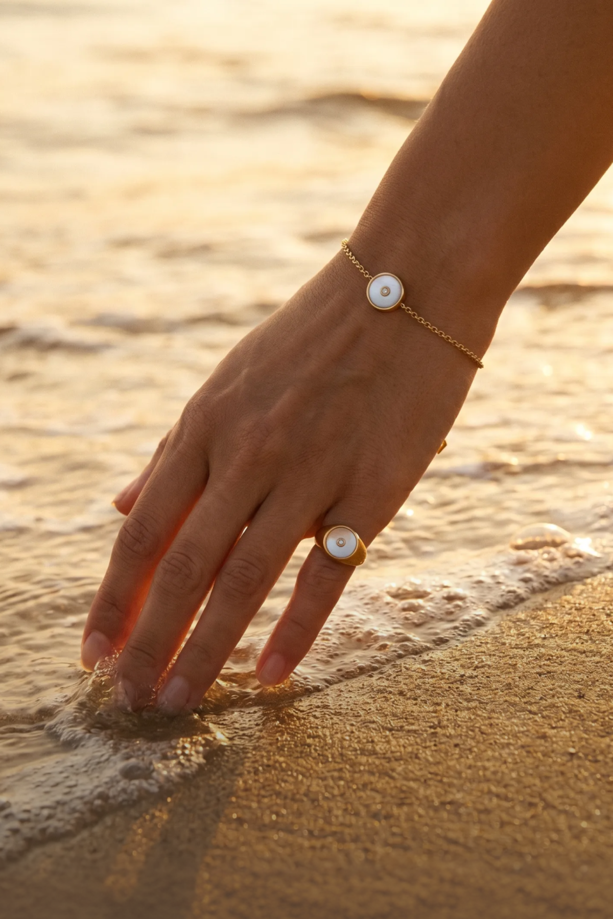 Model wearing the Minx Shell Bracelet and Signet Ring in 18K gold vermeil at the shoreline